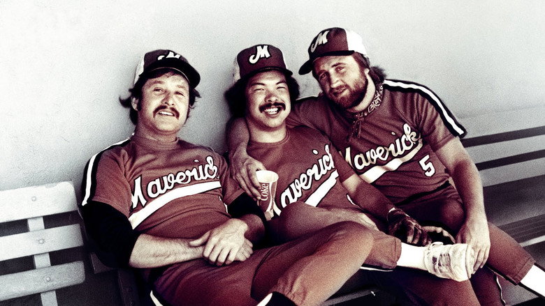 A grainy archival shot of the Portland Mavericks’ dugout, players in mismatched uniforms leaning against the railing, laughing