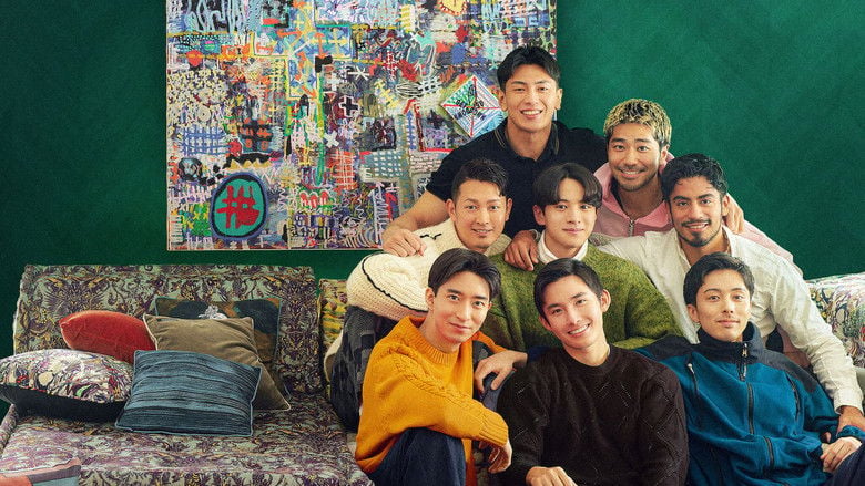 Nine men in casual clothes stand behind a coffee truck, laughing as one pours a drink