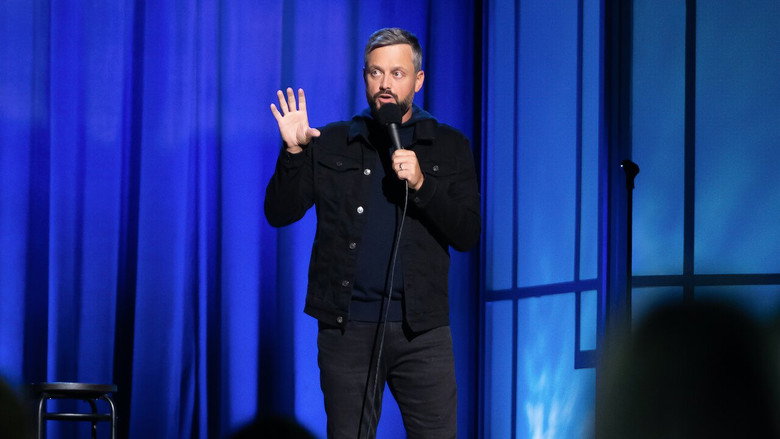 Nate Bargatze on stage, mid-gesture, under a warm spotlight