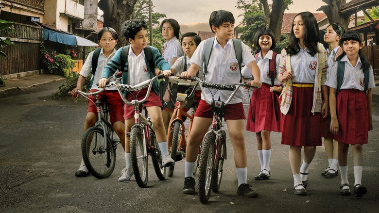 A classroom scene where Dilan and his friends sit in wooden desks, the warm light filtering through the windows, casting long shadows on the chalkboard behind them.