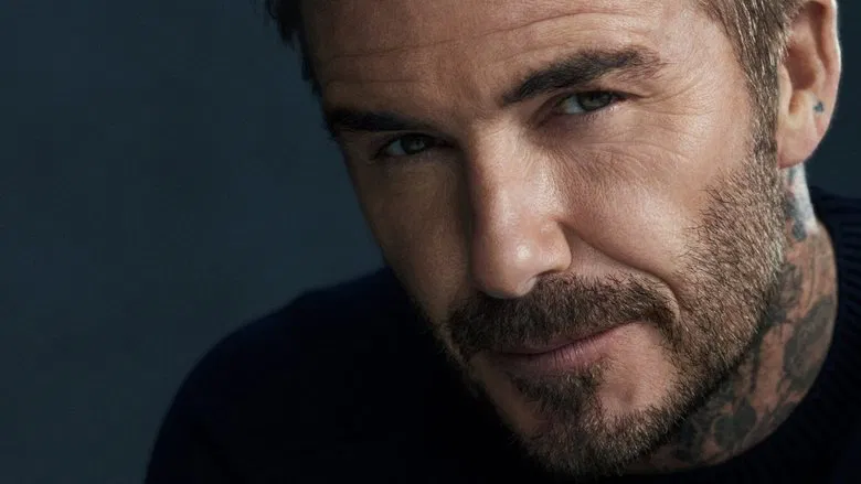 David Beckham watches footage of his younger self, his expression unreadable in the dim light of a screening room.