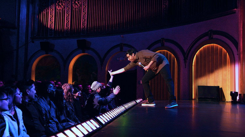 Hari Kondabolu on stage, mid-gesture, in a warmly lit theater