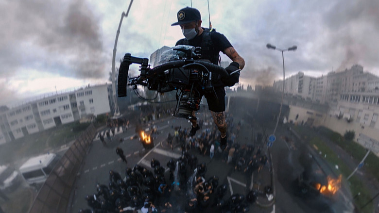 A camera operator suspended in midair, capturing a sweeping shot of a riot below