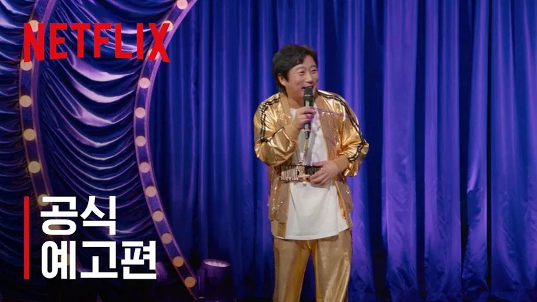 A dimly lit stage with a single spotlight, where Lee Su-geun stands at a podium, his expression caught between earnestness and performance.