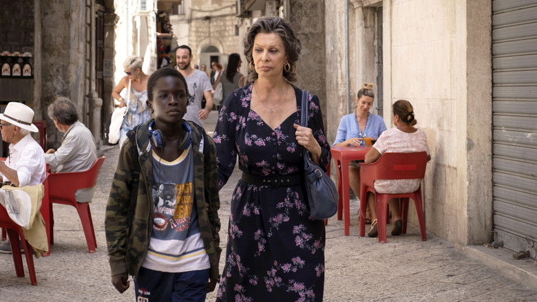 Madame Rosa and Momo walking along a sunlit Italian street, the sea visible in the background