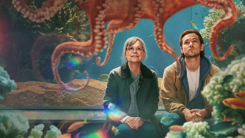 Tova and Cameron sit on opposite sides of a table in the aquarium’s dimly lit break room, the glow of the tank casting blue light across their faces.