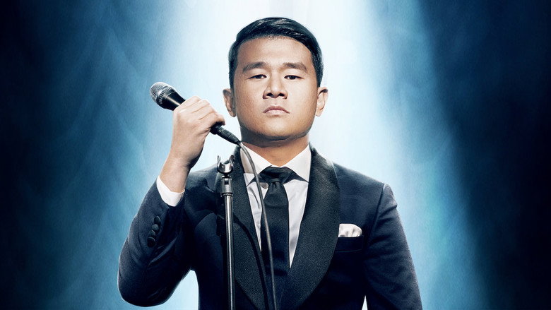 Ronny Chieng on stage, mid-gesture, his expression caught between amusement and exasperation