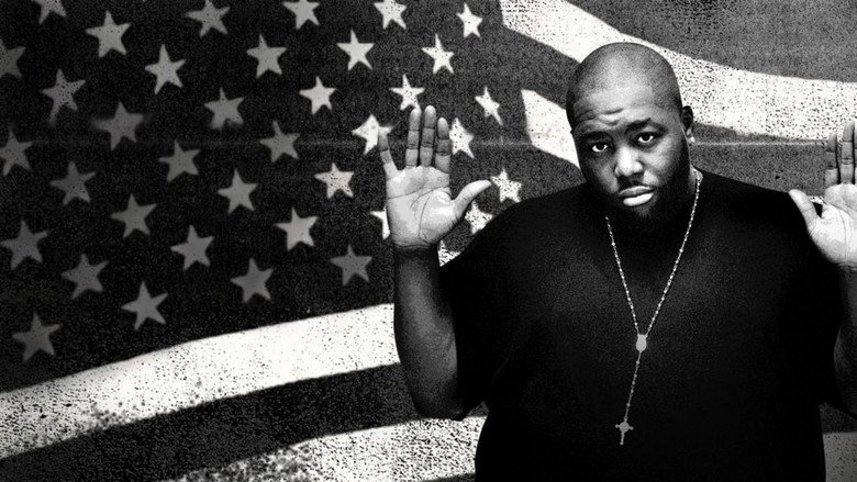 Killer Mike in a dimly lit room, his expression intense as he gestures while speaking