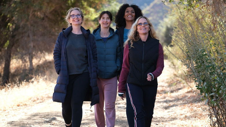 Four women sit around a table, laughing, but their expressions are layered with something unspoken.