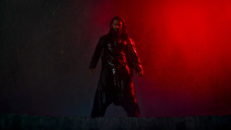A shadowy figure stands in the rain, his face half-lit by neon, a gun in his hand and a look of weary resolve.
