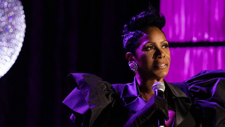 Sommore on stage, bathed in warm light, gesturing to the audience