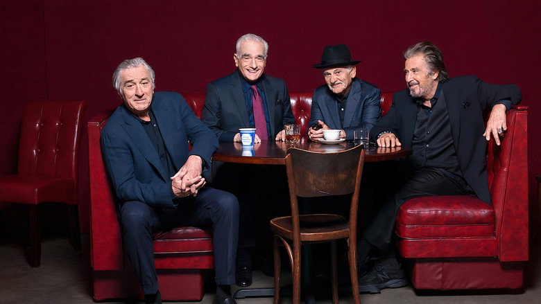 Four men seated in a dimly lit room, the glow of a lamp casting long shadows across their faces.