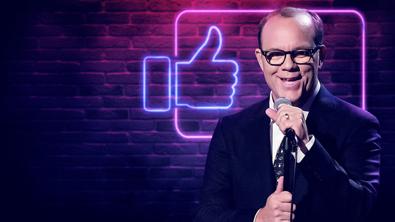 Tom Papa on stage, mid-gesture, in a bright suit against a warmly lit backdrop