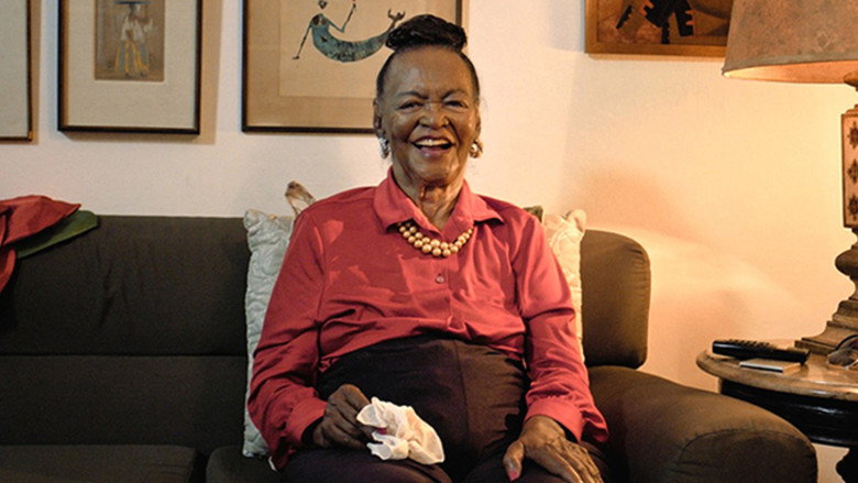 A close-up of Ruth de Souza's face, her expression unreadable yet weighted with decades of experience.