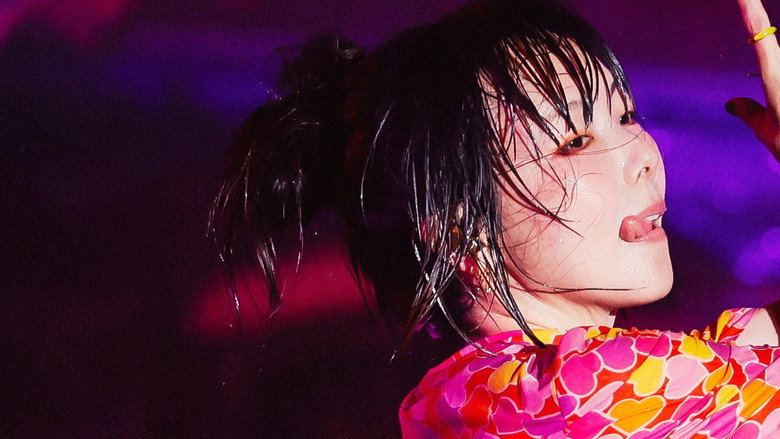 A stage bathed in golden light, the ocean stretching endlessly behind it, as aiko's silhouette stands center, microphone in hand.