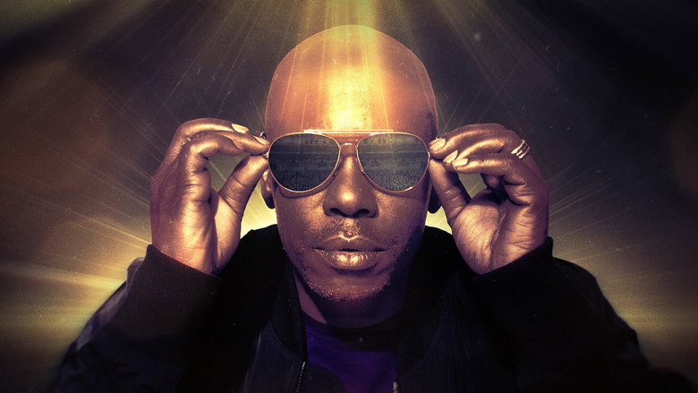 Chappelle on stage, mic in hand, mid-gesture, the crowd a blur of faces in the background