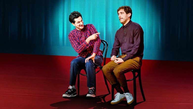 Two performers on stage, one mid-gesture, the other leaning in with a grin, the energy between them crackling.