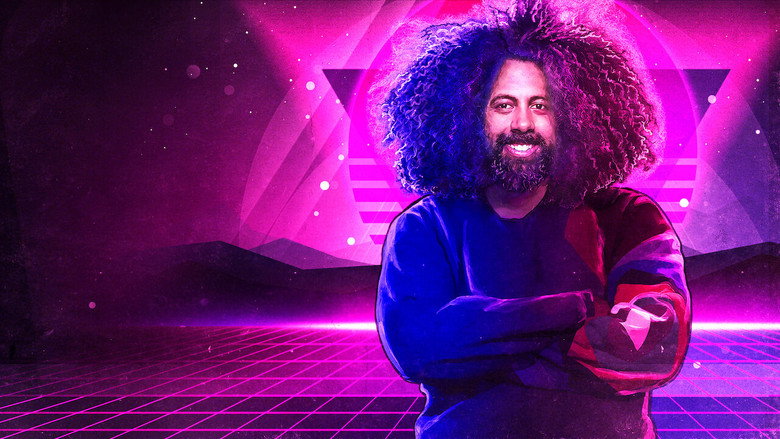 Reggie Watts on stage, bathed in blue light, mid-performance with a microphone in hand