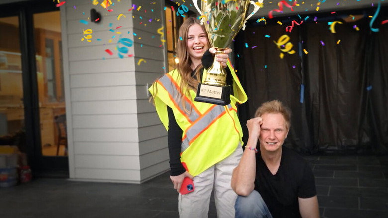 A brightly lit living room where Salish and Jordan stand side by side, grinning at the camera while holding a giant pair of scissors, mid-"challenge" setup.