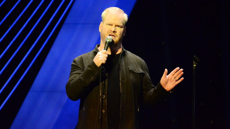 Jim Gaffigan on stage, mid-laugh, bathed in warm light