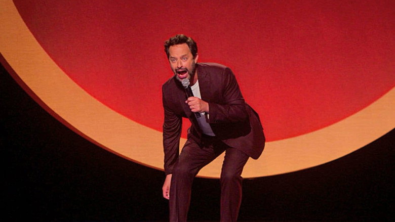 Nick Kroll on stage, mid-performance, gesturing with his hands as if explaining something profound—or maybe just trying to remember his next joke.
