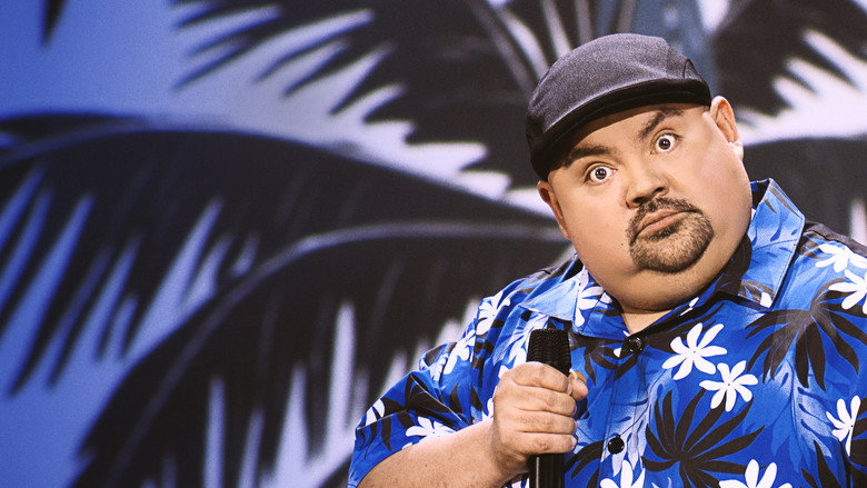 Gabriel Iglesias on stage, arms outstretched, grinning under bright lights