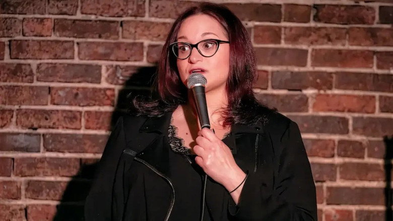 Adrienne Iapalucci on stage, bathed in a single spotlight, her expression unreadable as she delivers a punchline