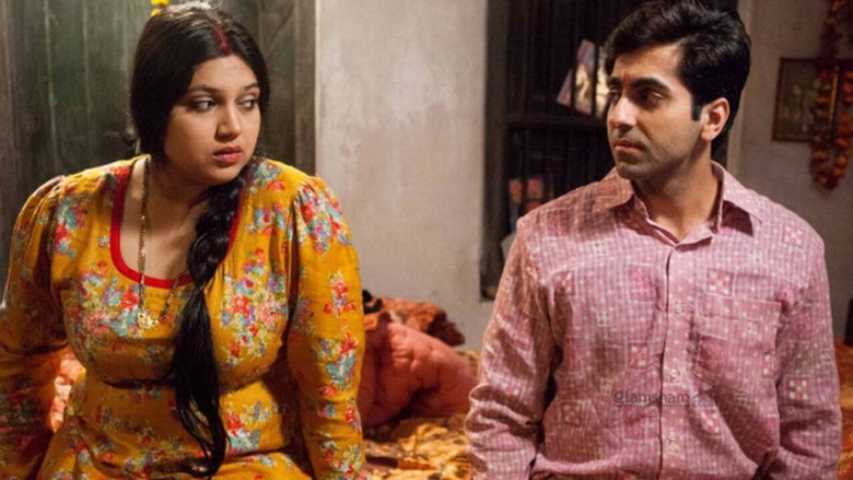A couple sits awkwardly on a bed, the tension between them palpable in the dim light