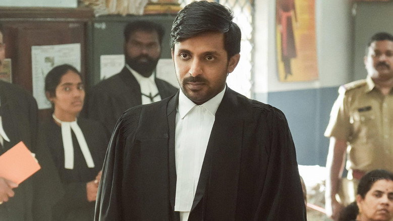 A dimly lit courtroom, the judge's bench looming over the defense table where Surya Teja sits, his posture slumped but his expression determined.
