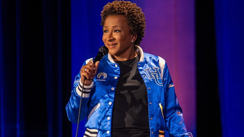 Wanda Sykes in a blue blazer, mid-laugh on stage, with a Hampton University backdrop