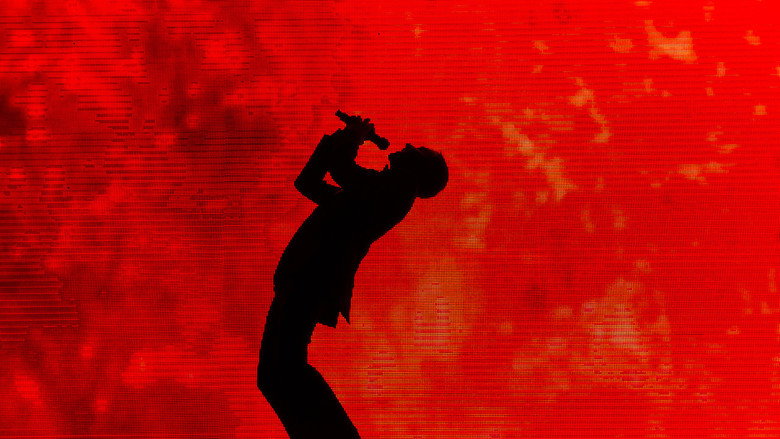 Aziz Ansari on stage at Madison Square Garden, bathed in blue light, mid-performance
