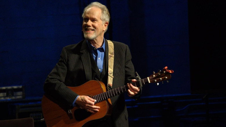 Loudon Wainwright III on stage, guitar in hand, mid-song