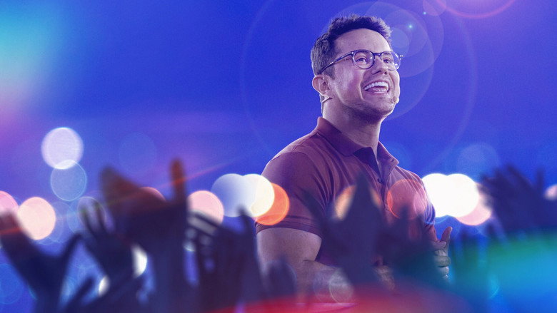 A dimly lit stage, bathed in soft blue light, with Deive Leonardo standing at a microphone, his posture relaxed but attentive.