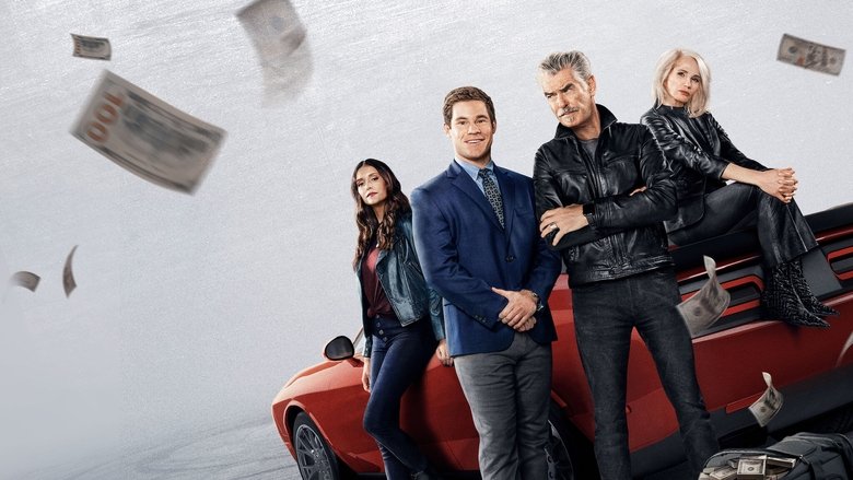 A frantic Adam Devine in a bank vault, surrounded by chaos, as Pierce Brosnan’s character watches with amused detachment