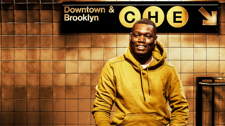 Michael Che onstage, mid-joke, with a smirk that suggests he knows exactly how uncomfortable he’s making the audience.