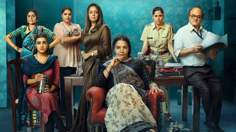 Five women in saris stand in a dimly lit alley, their faces half-shadowed, the glow of a streetlamp catching the edges of their tiffin carriers.