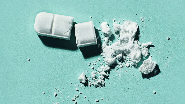 A close-up of a hand holding a blister pack of small white pills, the word "XANAX" barely visible on each one