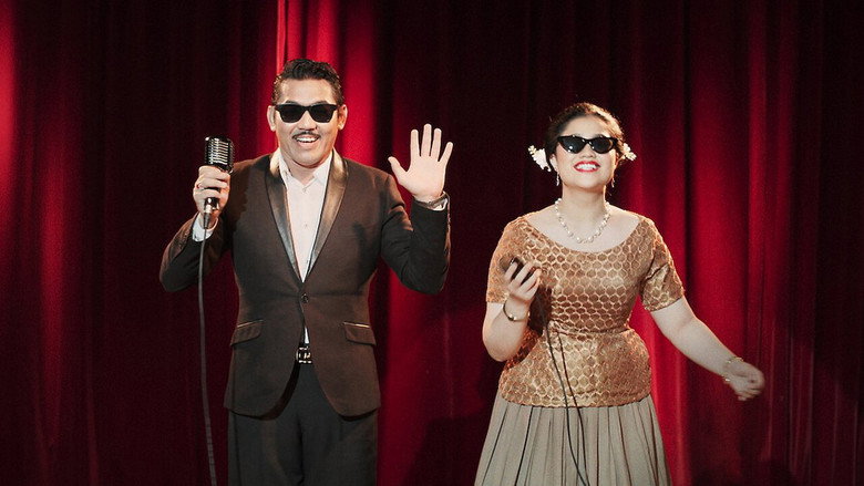 A dimly lit soundstage, bathed in the warm glow of stage lights, with props and set pieces scattered in the background, evoking the nostalgia of 1950s Malay cinema.