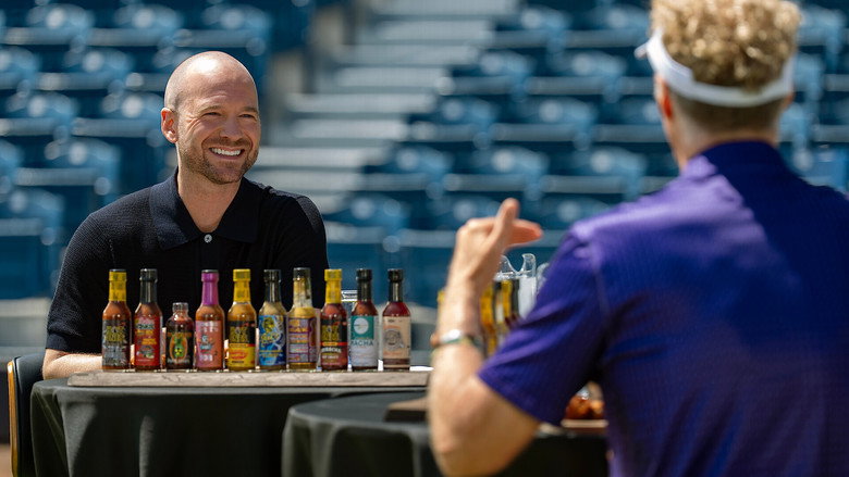 Sean Evans and Will Ferrell mid-interview, Ferrell's face flushed, a wing halfway to his mouth, the stadium lights casting long shadows