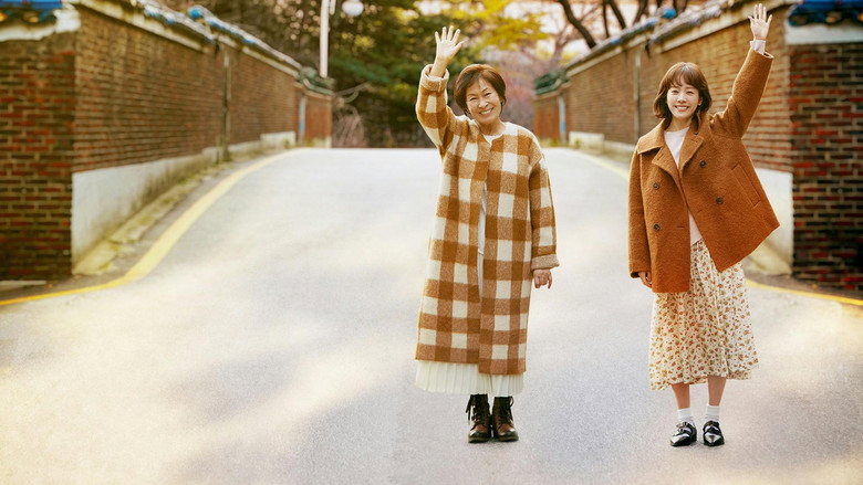 A dimly lit room where Kim Hye-ja, now elderly, sits alone at a table, her reflection fractured in a mirror.