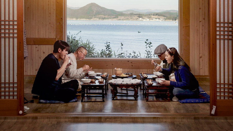 A close-up of hands arranging small dishes of banchan on a wooden table, steam rising from a bowl of rice