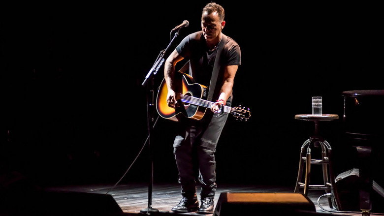 Bruce Springsteen on stage at the Walter Kerr Theatre, bathed in warm light, guitar in hand.