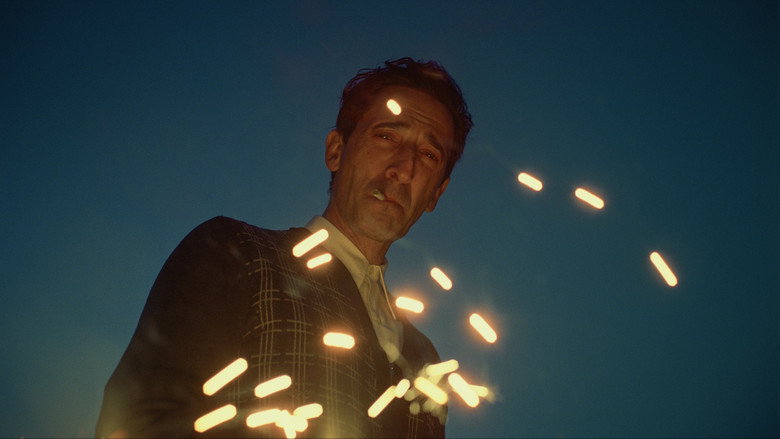 A stark, geometric shot of Adrien Brody standing in the skeletal frame of a half-built modernist structure, his face half in shadow.