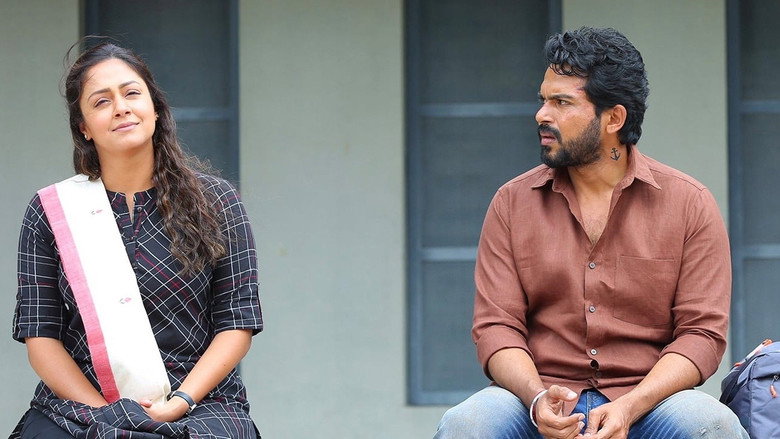 A tense family dinner scene, with Vicky (Karthi) seated at the table, his expression unreadable as the family watches him with suspicion.