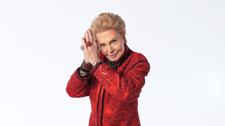 Walter Mercado in a sunlit room, draped in a jewel-toned cape, adjusting a ring on his finger