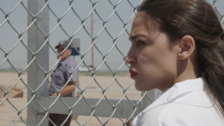 AOC stands in front of a campaign poster, her face lit by the glow of a phone screen as she reads a message.