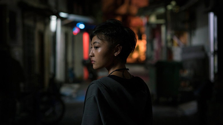 A neon-lit cybercafe at night, its glow reflecting off the faces of exhausted workers