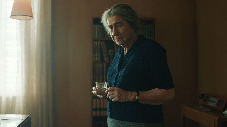 Golda Meir, played by Helen Mirren, sits in a dimly lit war room, surrounded by advisors, with cigarette smoke curling around her face.