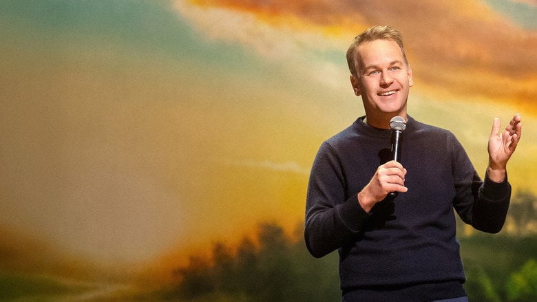 Birbiglia on stage, mid-gesture, under a warm spotlight