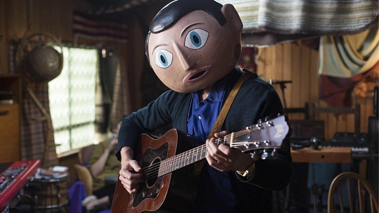 The band Soronprfbs performs in a dimly lit room, Frank's giant head looming over the chaos